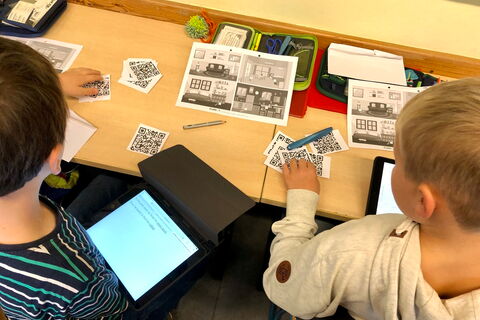 Kinder mit Zetteln und Tablet am Schreibtisch